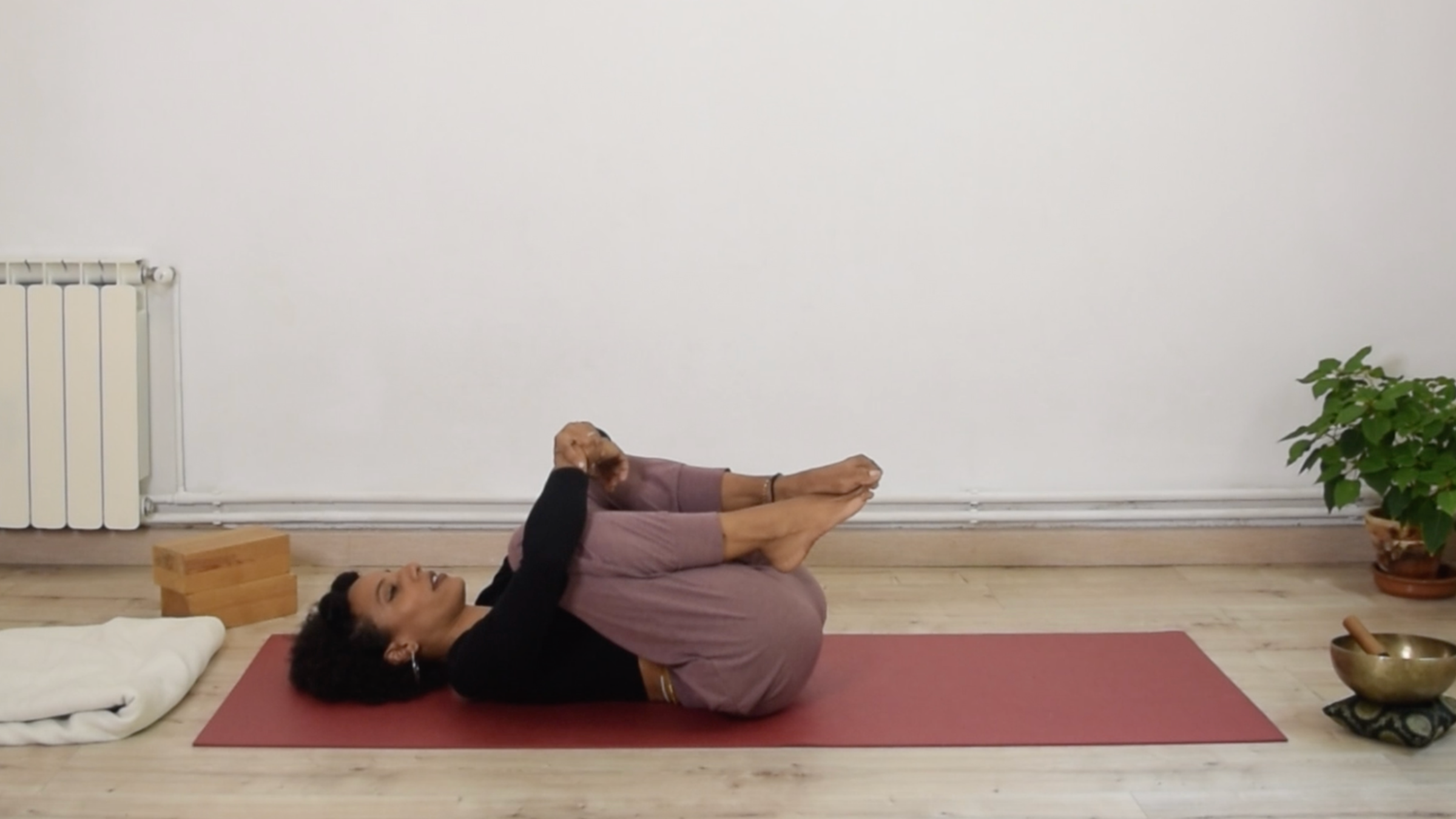 Yoga instructor Laia Bové lying flat on her back while hugging both knees into her chest in Wind-Relieving Pose.